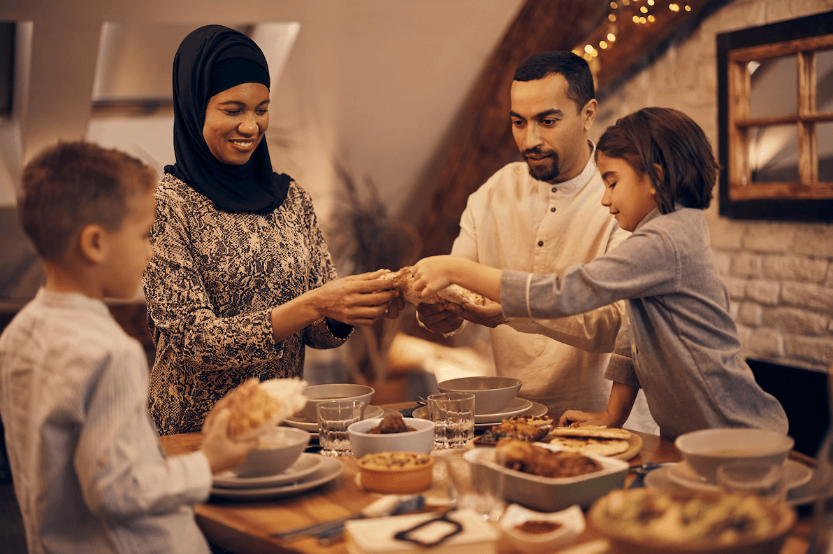 Traditional Muslim parents and their kids sharing pita bread during family dinner on Ramadan. In 2024, Ramadan begins in March and runs through until April.